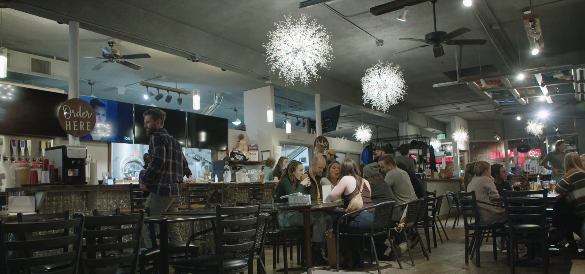 Brewability's dining room, full of customers at tables under large starburst light fittings, with the order counter at the back.