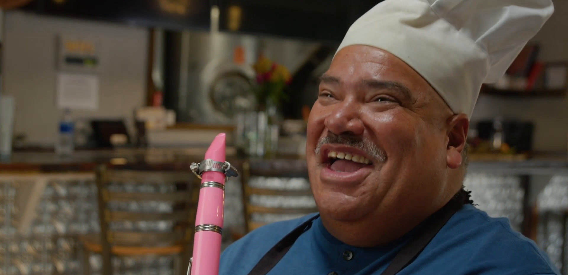 Jorge in a chef's hat and apron, smiling with his bright pink clarinet.
