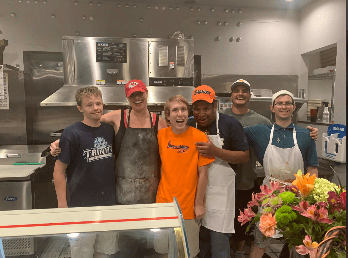 Six Pizzability crew members smiling together in the restaurant kitchen.