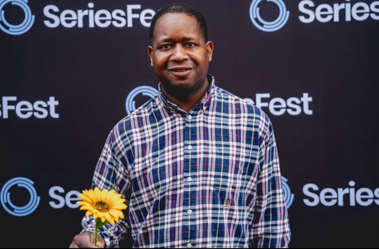 Aaron standing in front of a SeriesFest backdrop and holding a yellow flower.