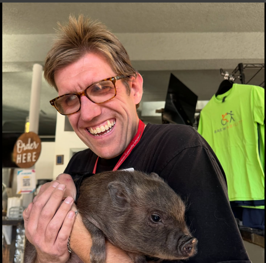 Alex smiling broadly while holding a small piglet inside Brewability.