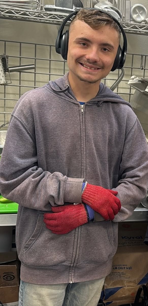 Ethan smiling in the Brewability kitchen, wearing headphones and red work gloves.