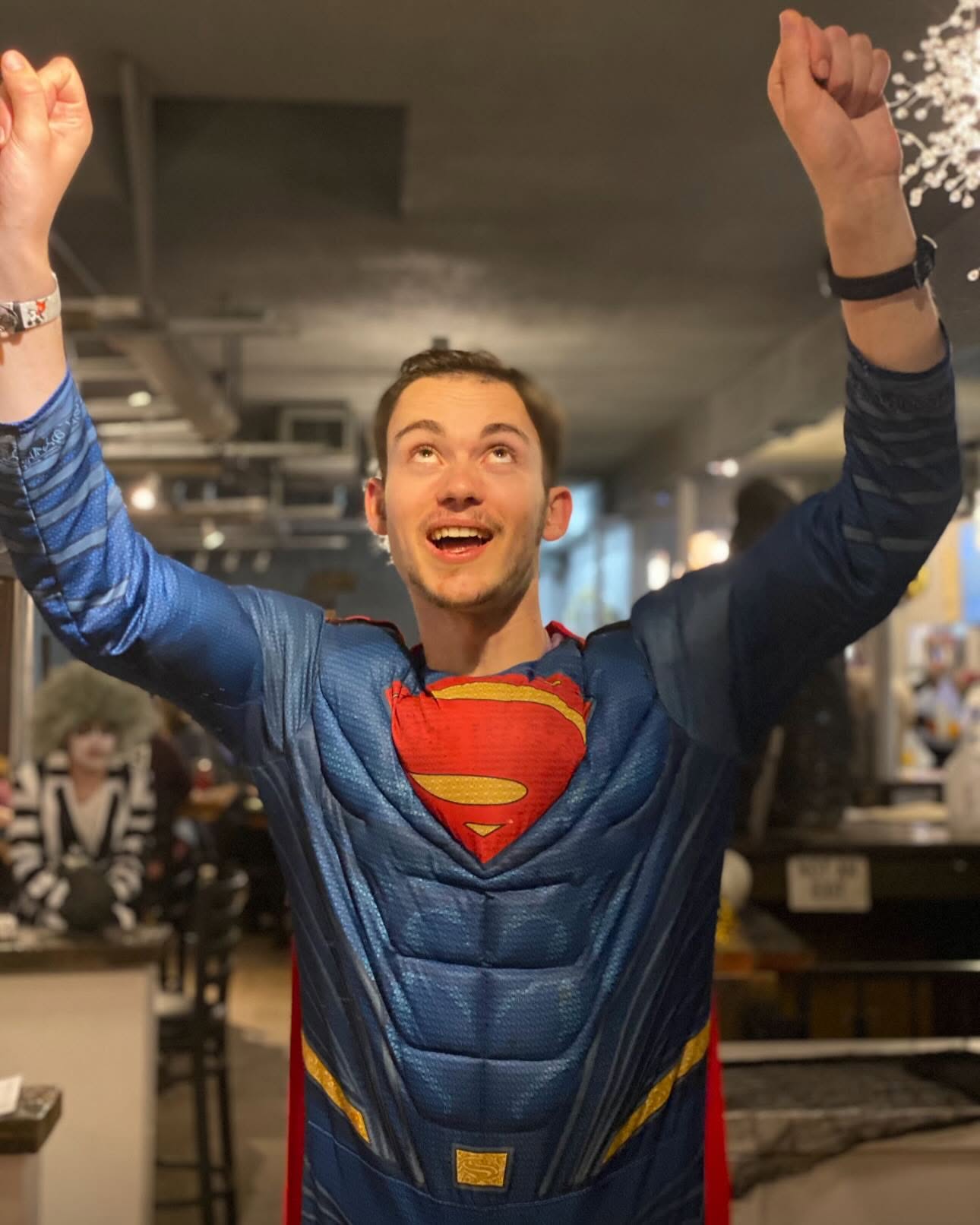 Michael smiling in a Superman costume with both arms raised inside Brewability.