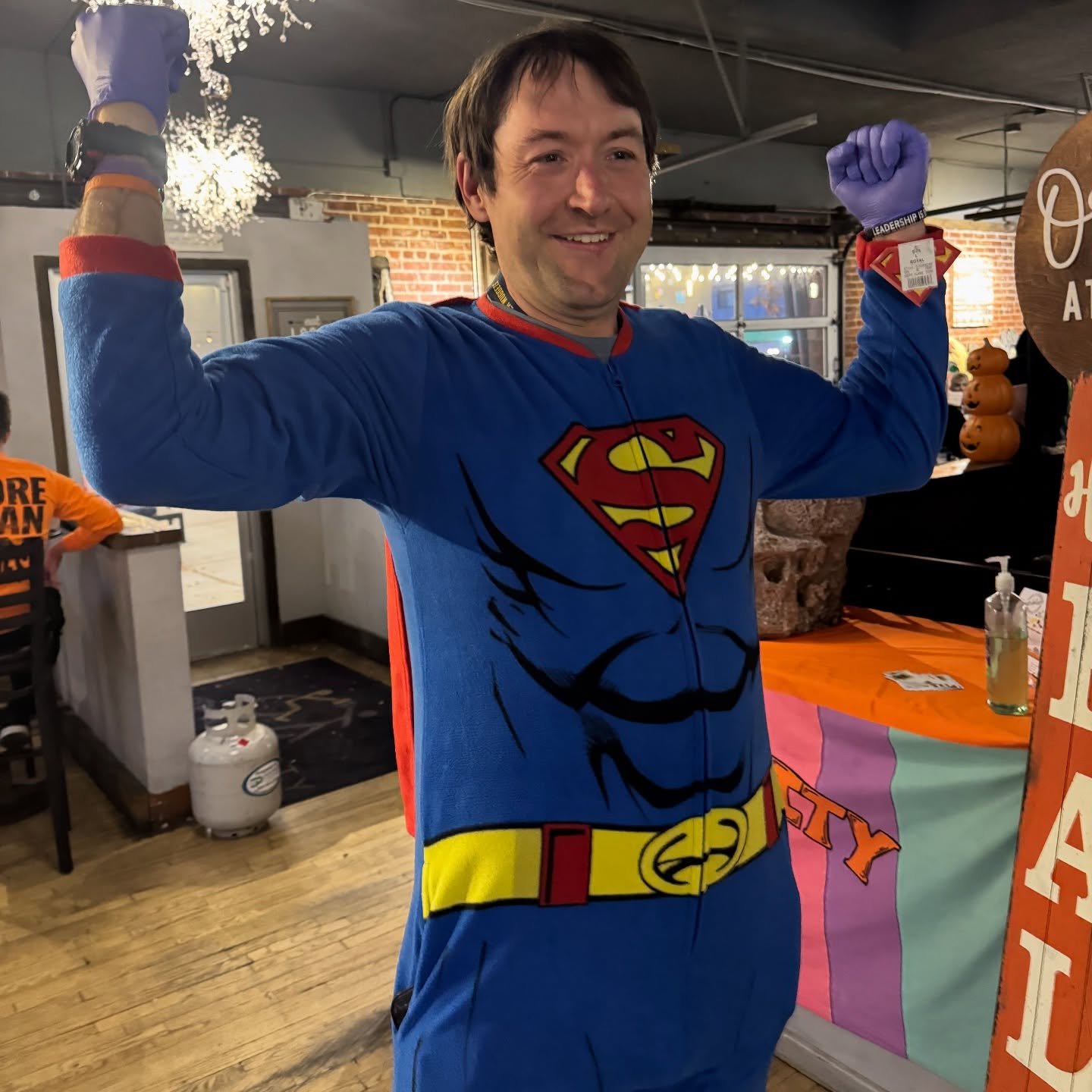Nathan smiling in a Superman costume with both arms raised at Brewability.